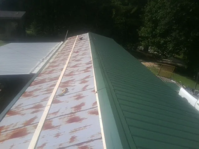 Old rusted panels beside newly installed green metal roofing — Wind Damage Roof Repair by Roofing Brothers in Gadsden