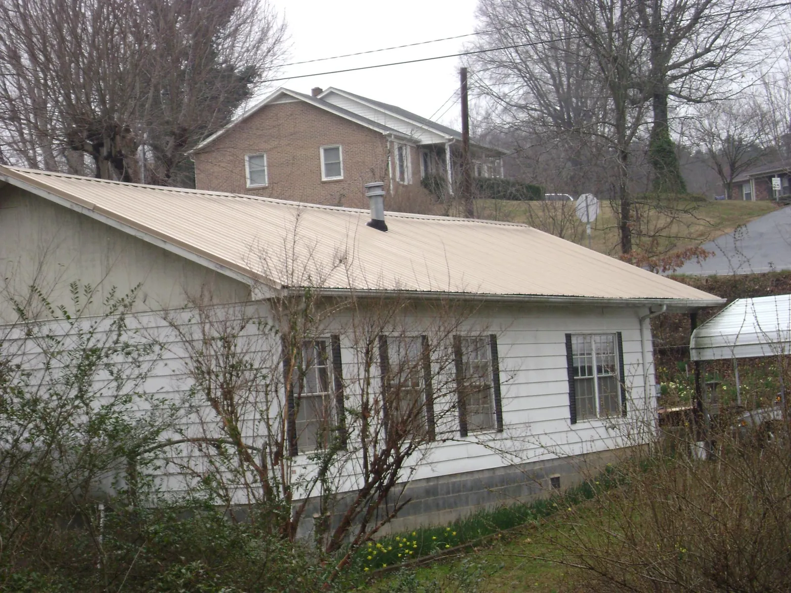 Tan metal roof on a white sided house set into a hillside — Commercial Roofing by Roofing Brothers in Gadsden